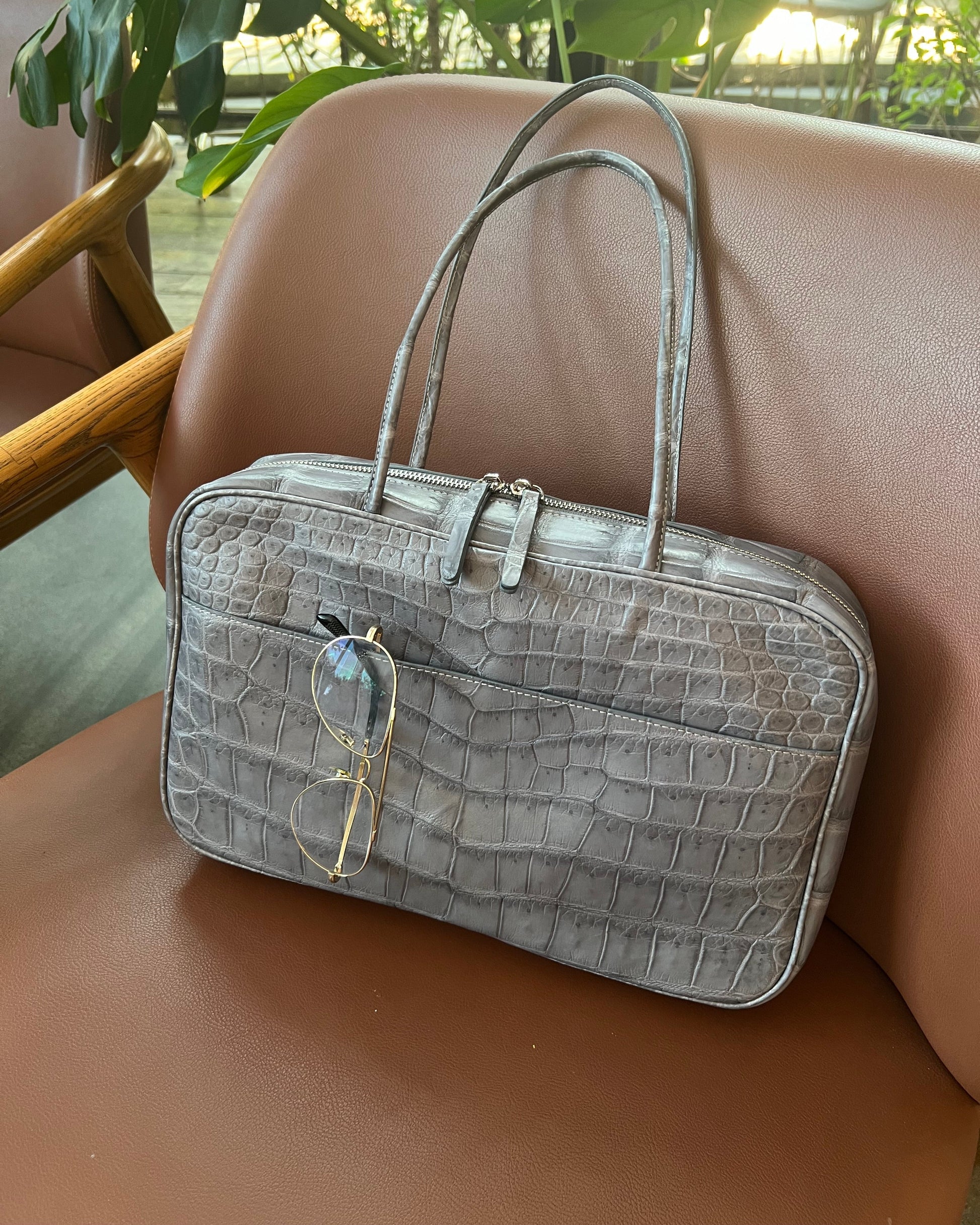 Gray textured handbag with a pair of glasses on a brown surface