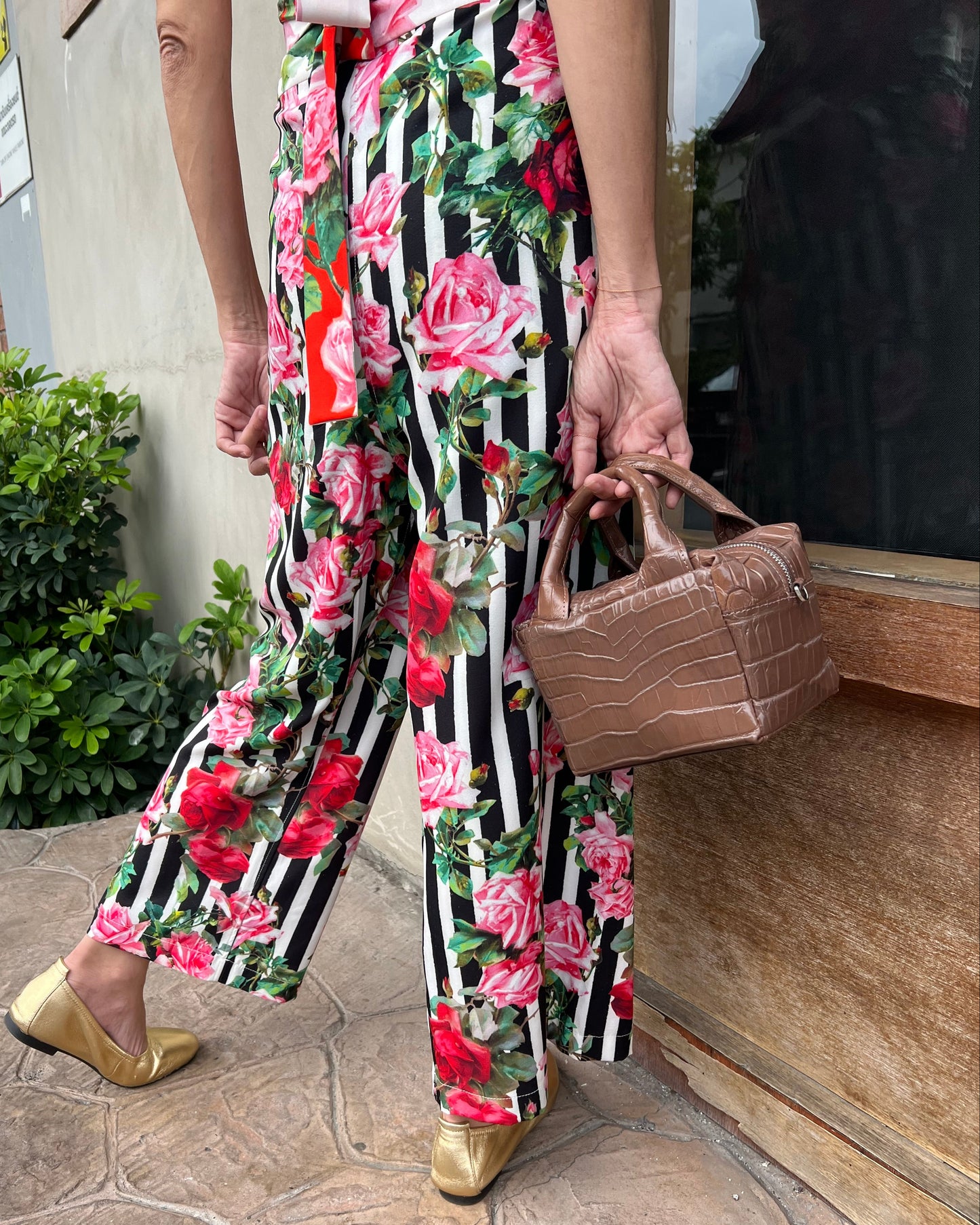 Person wearing a floral and striped dress with a brown bag, standing on a stone pavement.