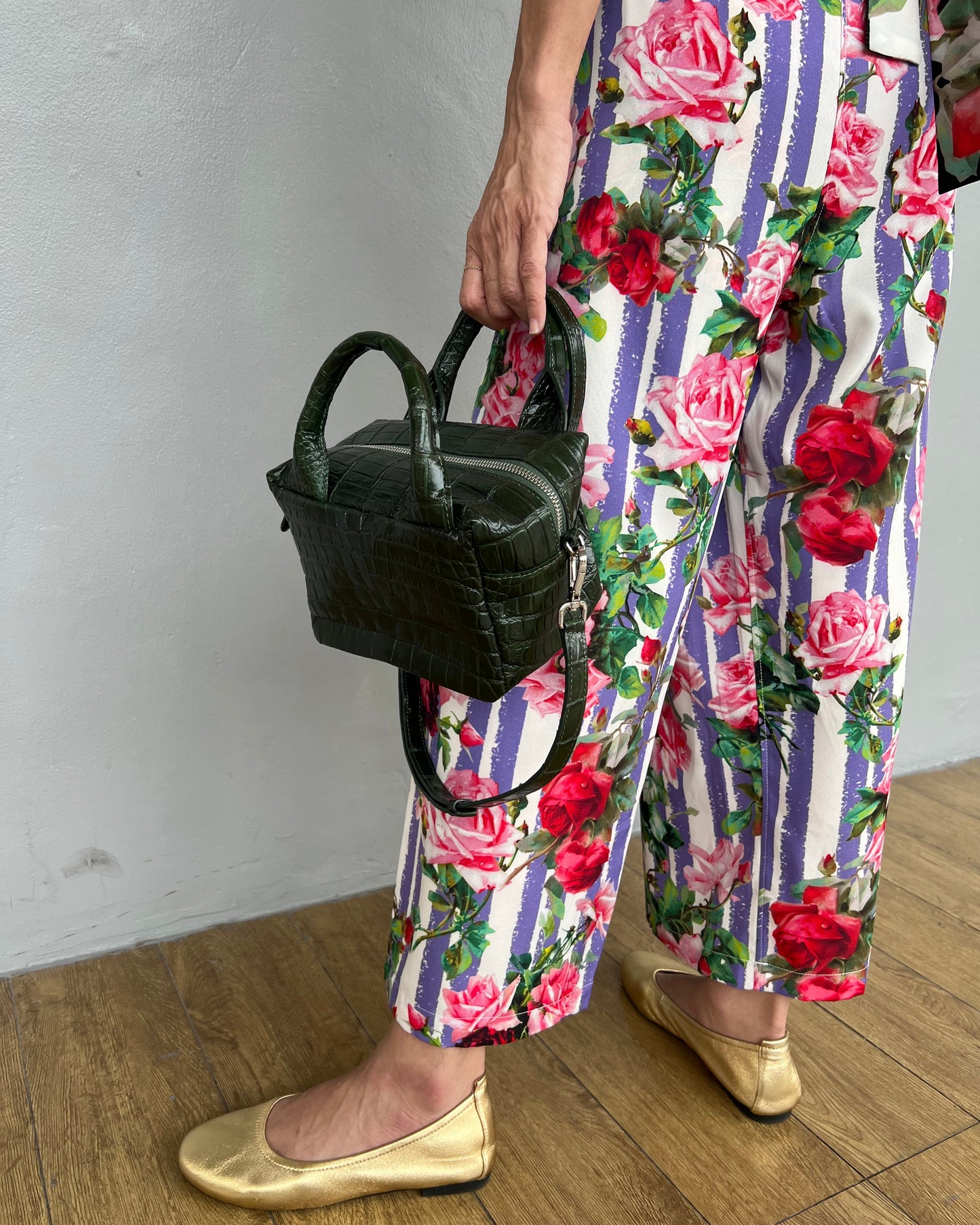 Person wearing floral pants with stripes and holding a black bag on a white floor.