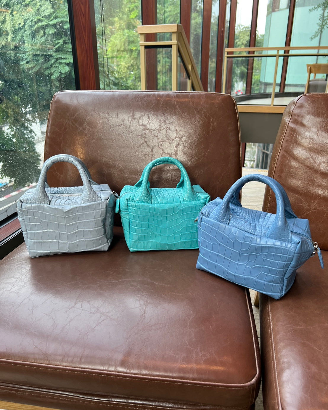 Three small handbags in gray, turquoise, and blue on a brown leather chair.