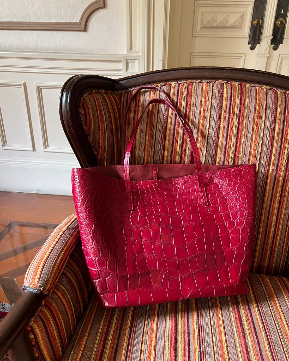 Red textured handbag on a striped sofa with a decorative wall in the background