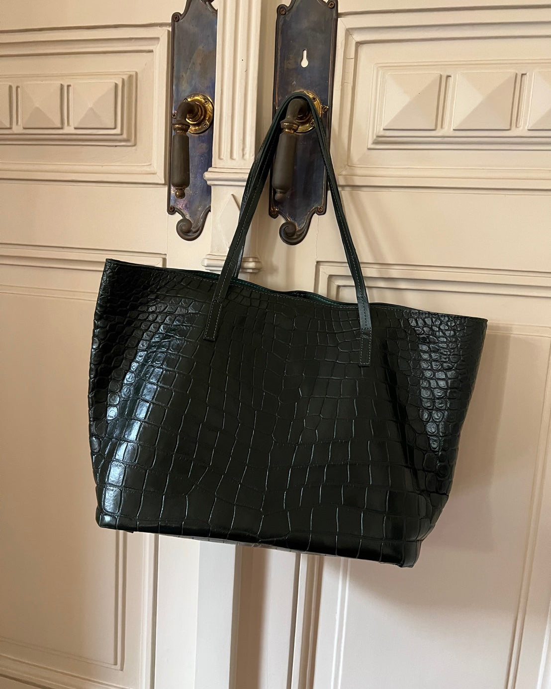 Black textured tote bag hanging on a door handle against a white paneled wall.