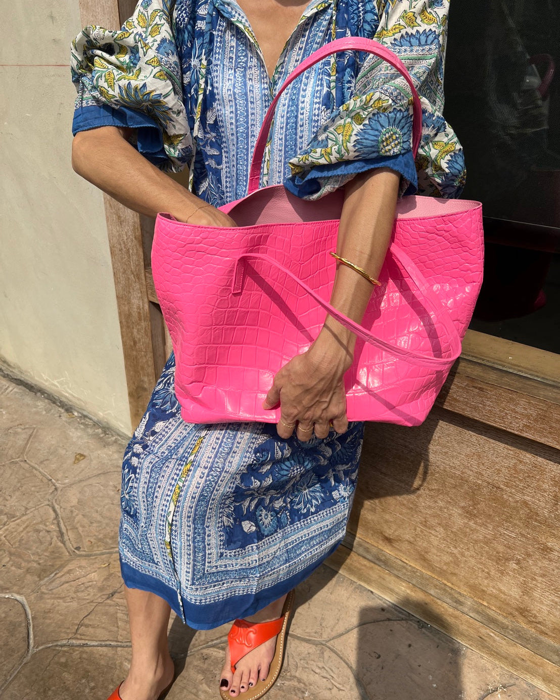 Person holding a pink bag outdoors on a wooden surface