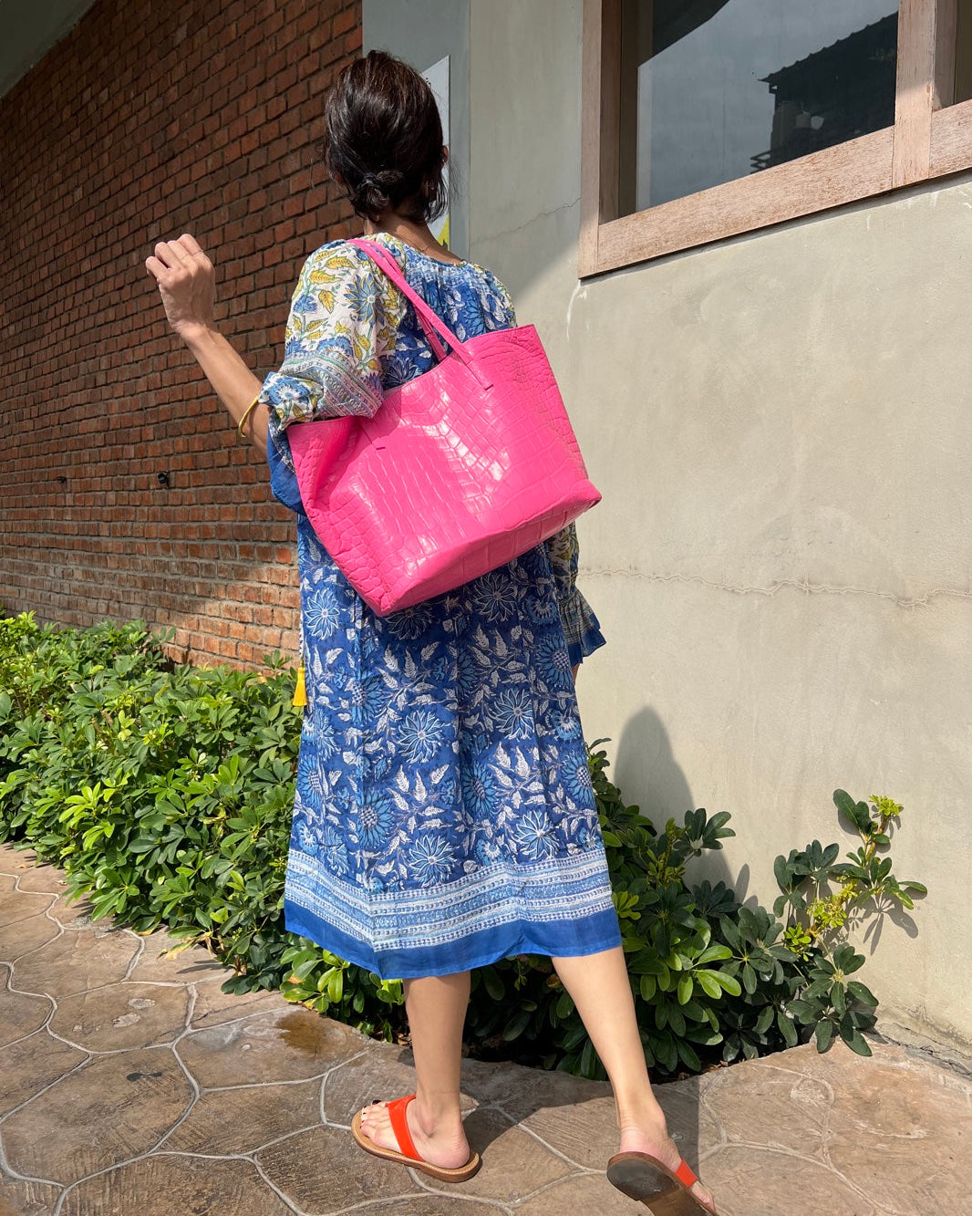 Person wearing a blue dress and carrying a pink bag, walking outdoors.