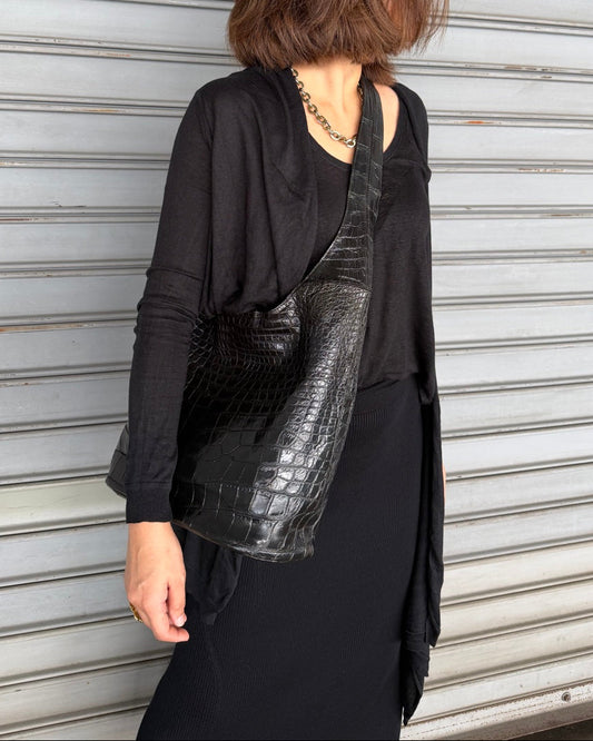 Person wearing a black outfit with a shiny black bag against a metallic shutter background